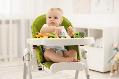 Photo of Children toys. Cute little boy playing with toy cars in high chair at home