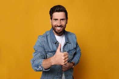 Photo of Handsome bearded man showing thumb up on orange background
