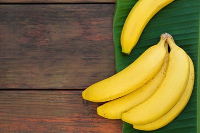 Photo of Delicious bananas and green leaf on wooden table, top view. Space for text