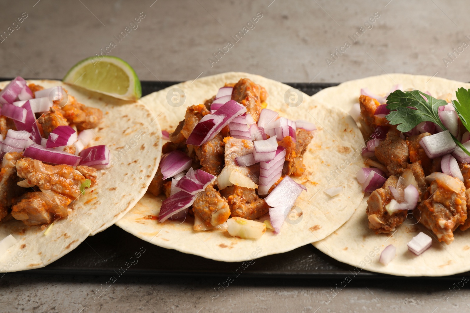 Photo of Delicious tacos with vegetables and meat on grey textured table, closeup