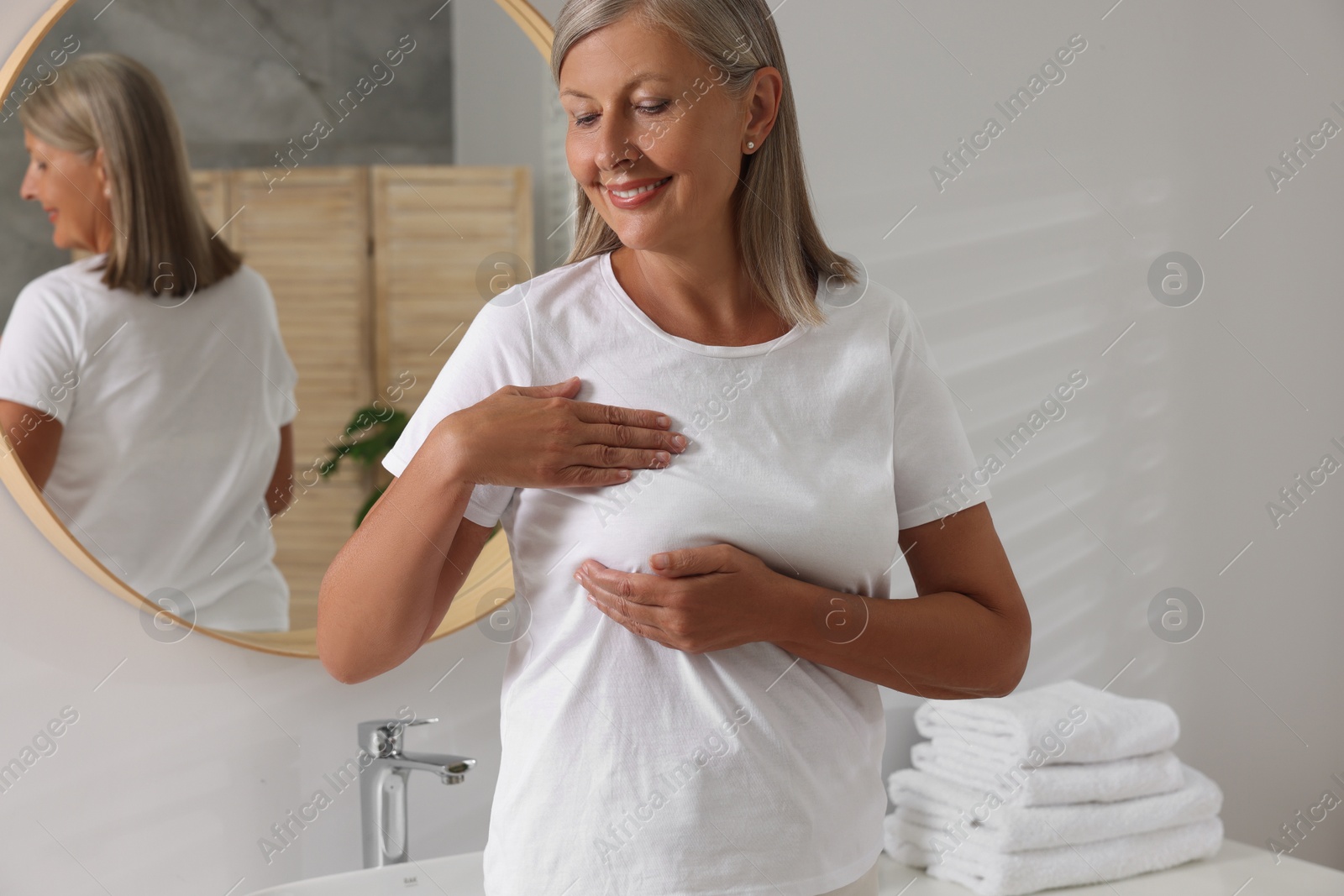 Photo of Beautiful senior woman doing breast self-examination in bathroom