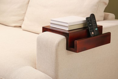 Books and remote controls on sofa armrest wooden table in room. Interior element