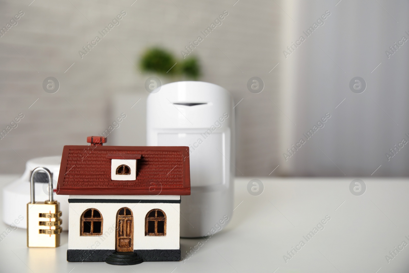 Photo of House model, lock, smoke and movement detectors on table in room, space for text. Home security system