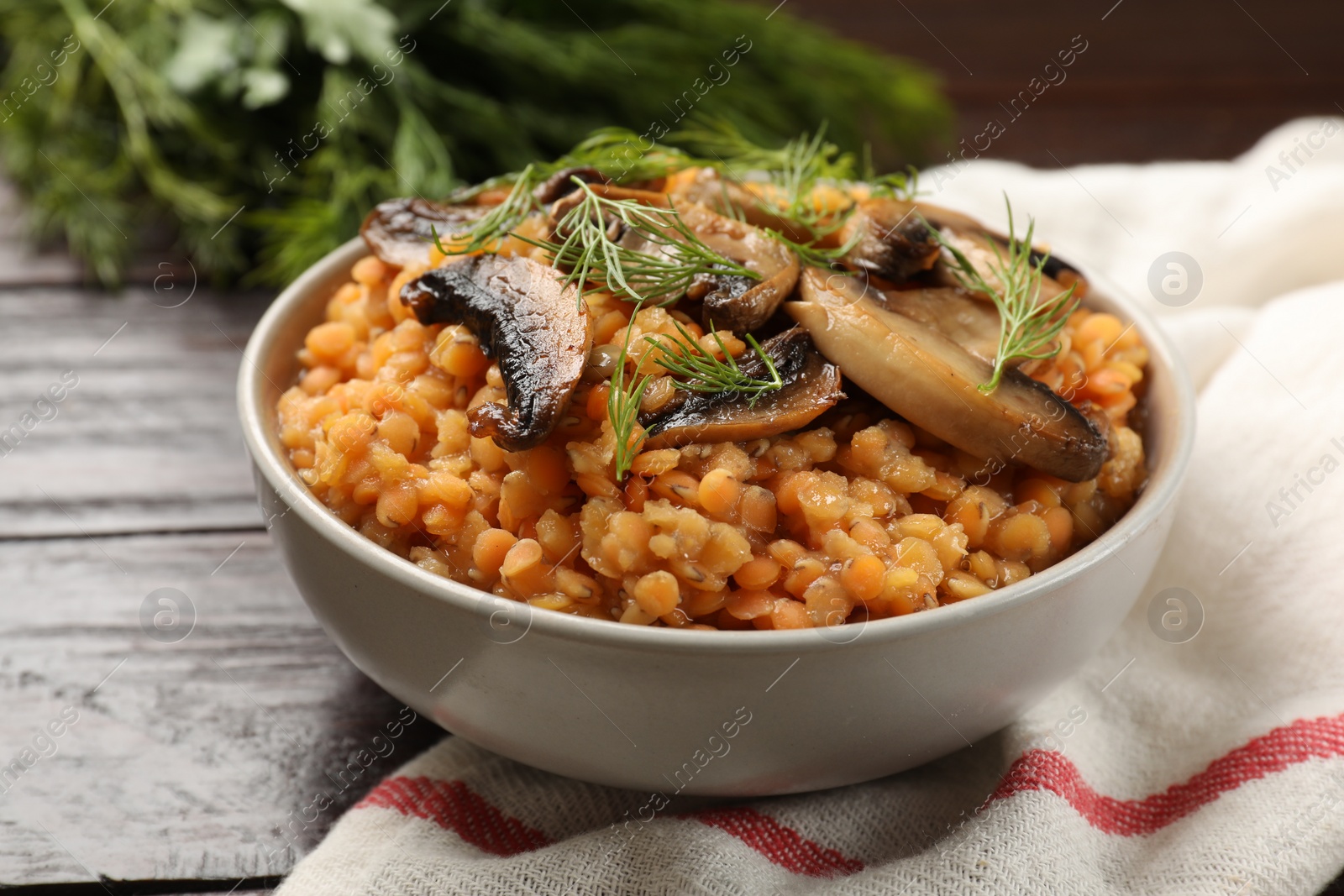 Photo of Delicious red lentils with mushrooms and dill in bowl on table, closeup