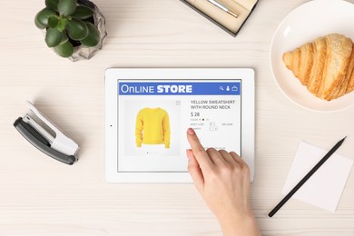 Woman with tablet shopping online at white wooden table, top view