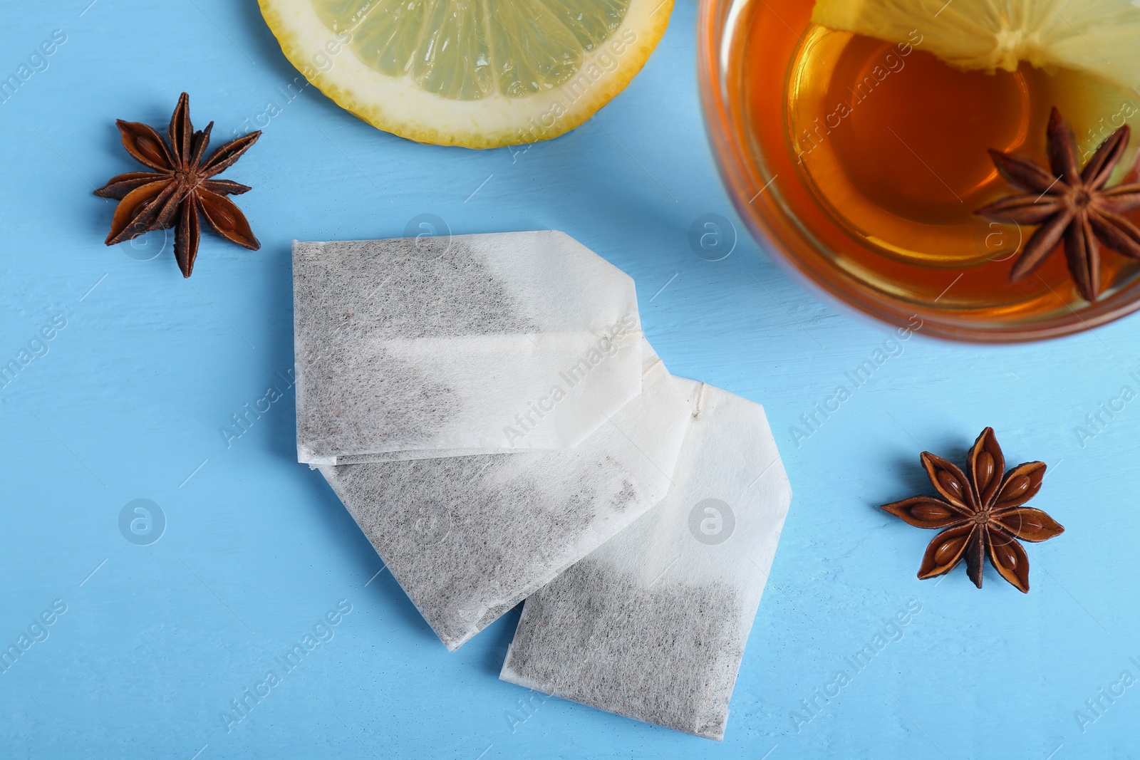 Photo of Tea bags, cup of hot drink, anise stars and lemon on light blue wooden table, flat lay