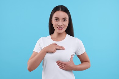 Beautiful happy woman doing breast self-examination on light blue background