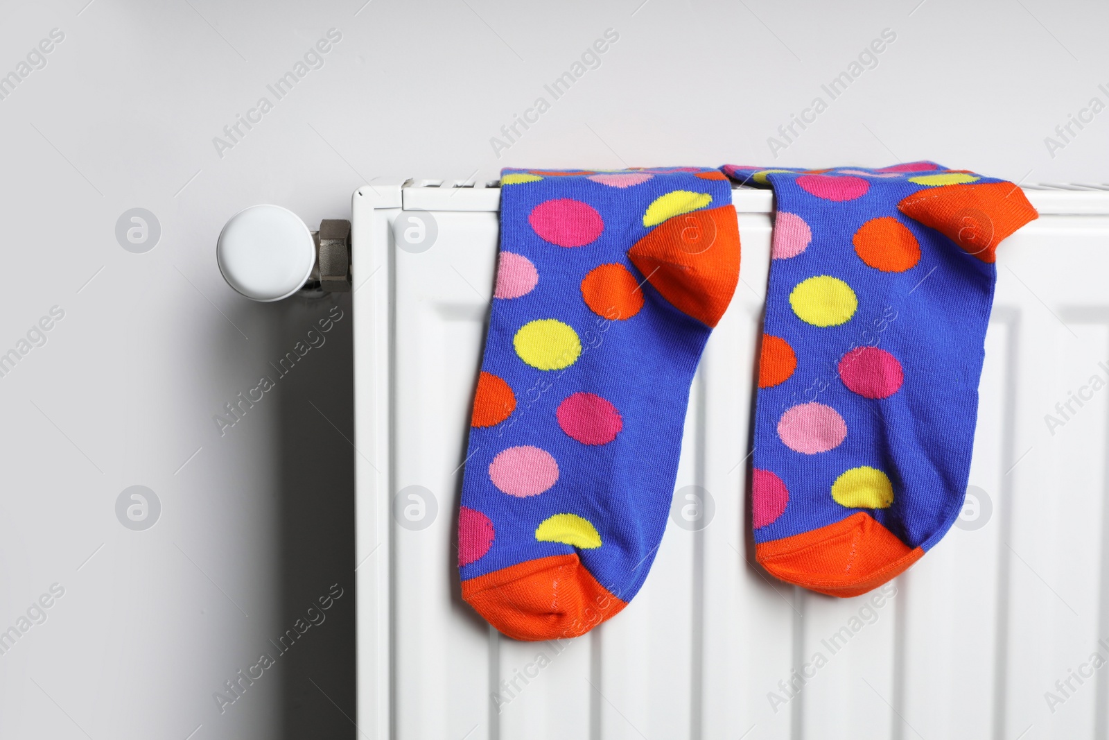 Photo of White radiator with colorful socks on light wall