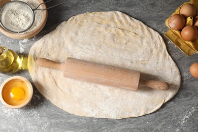 Photo of Raw dough, rolling pin and ingredients on grey table, flat lay