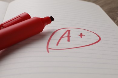 Photo of School grade. Red letter A with plus symbol on notebook paper and marker, closeup