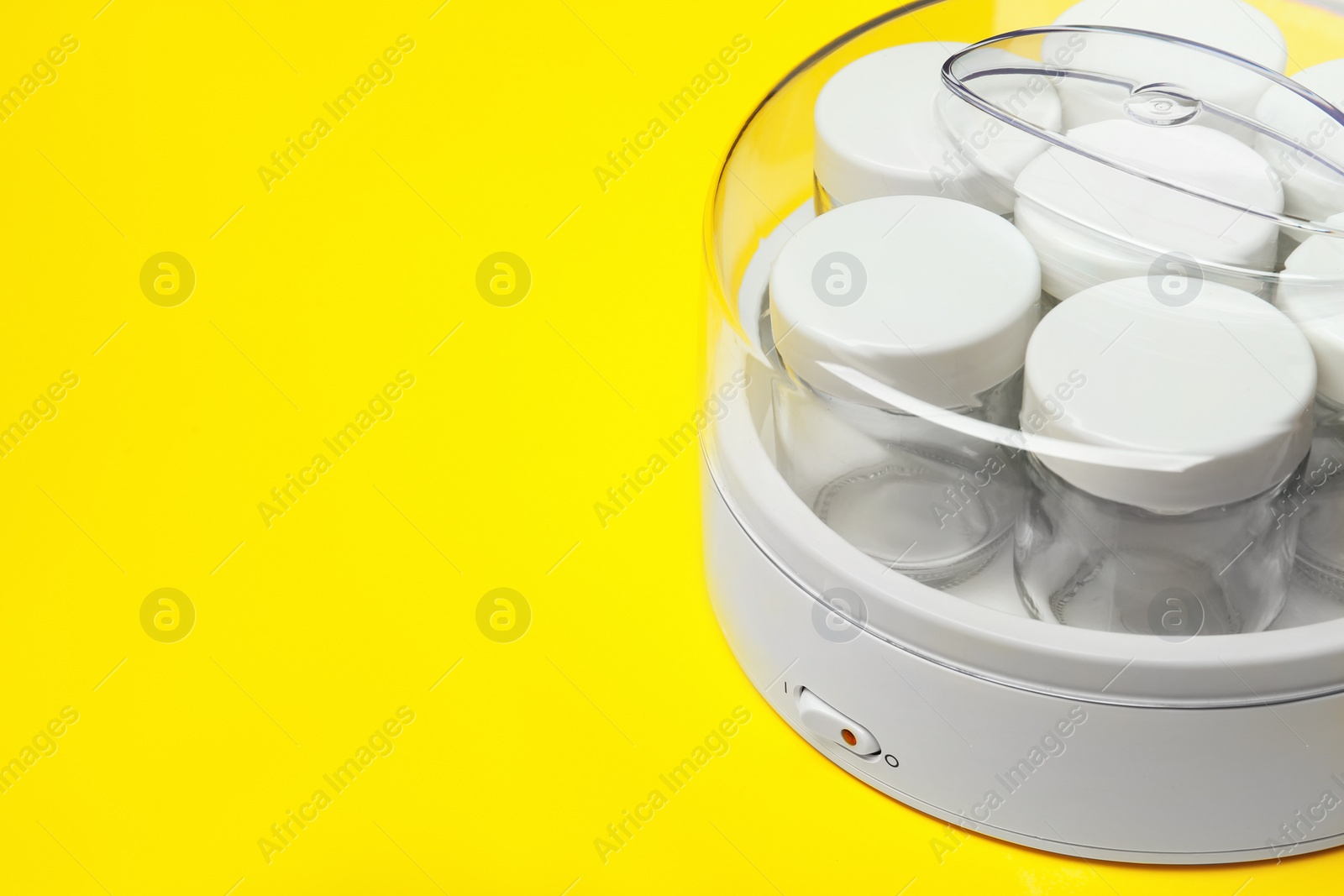 Photo of Modern yogurt maker with empty jars on yellow background, closeup. Space for text