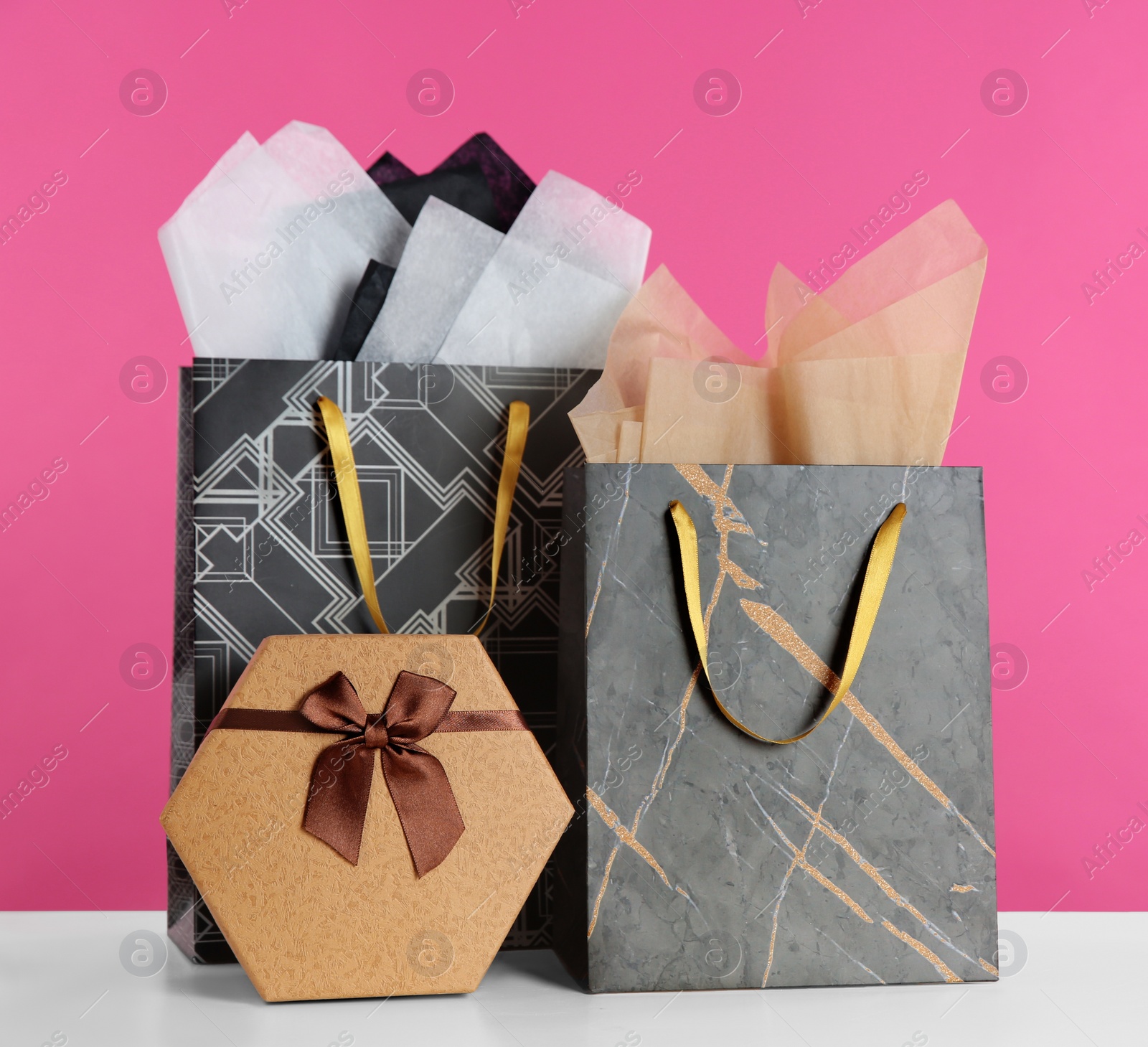 Photo of Gift bags with paper on white table against pink background