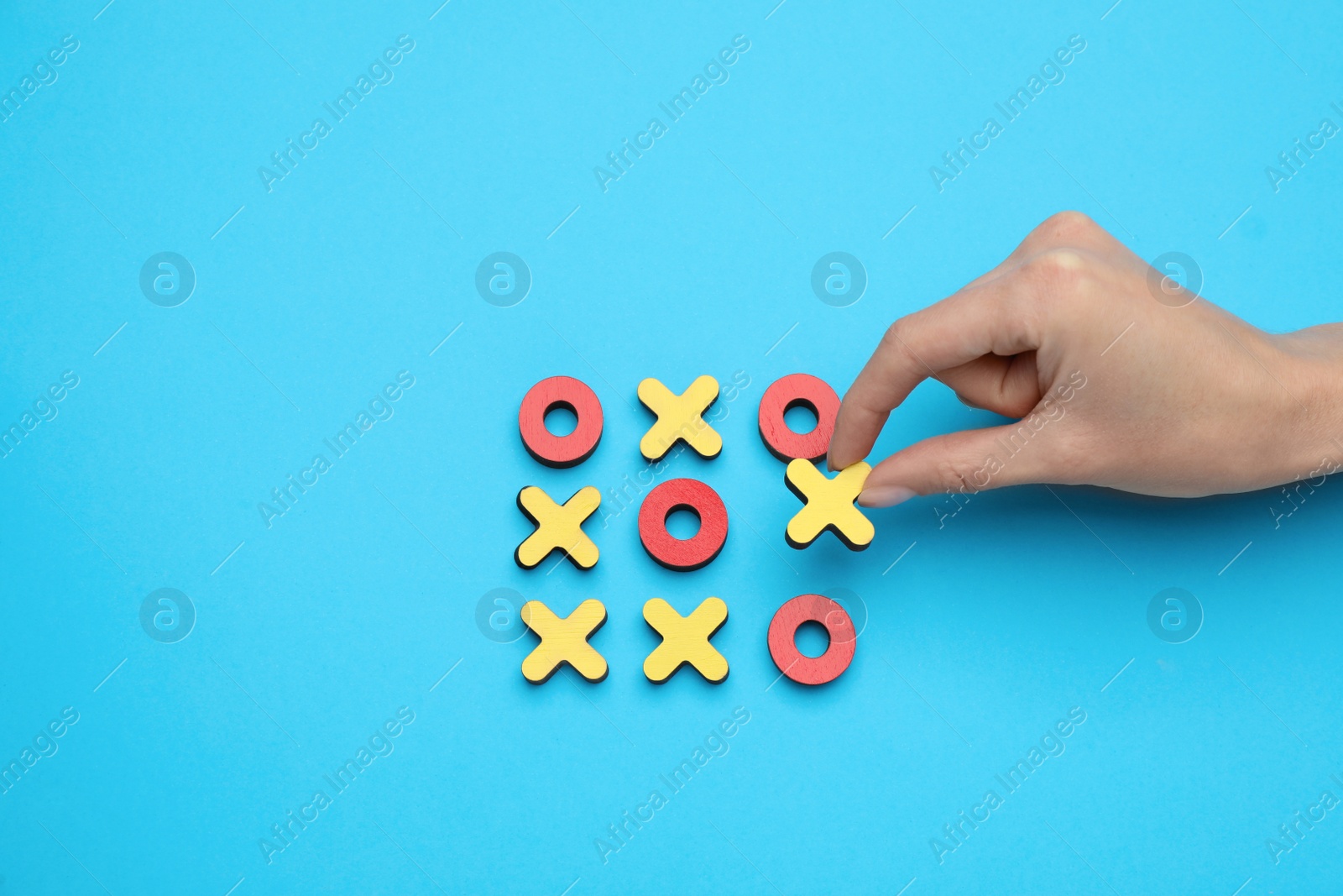 Photo of Woman playing tic tac toe game on light blue background, top view