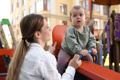 Photo of Happy nanny and cute little boy on seesaw outdoors