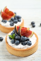 Photo of Tarts with blueberries and figs on white wooden table. Delicious pastries