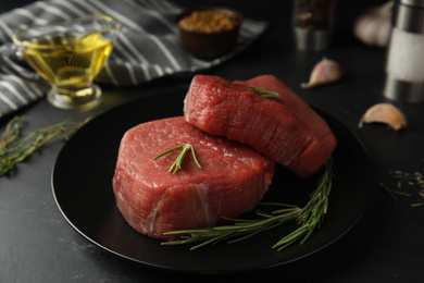 Photo of Fresh raw beef cut with rosemary on black table, closeup