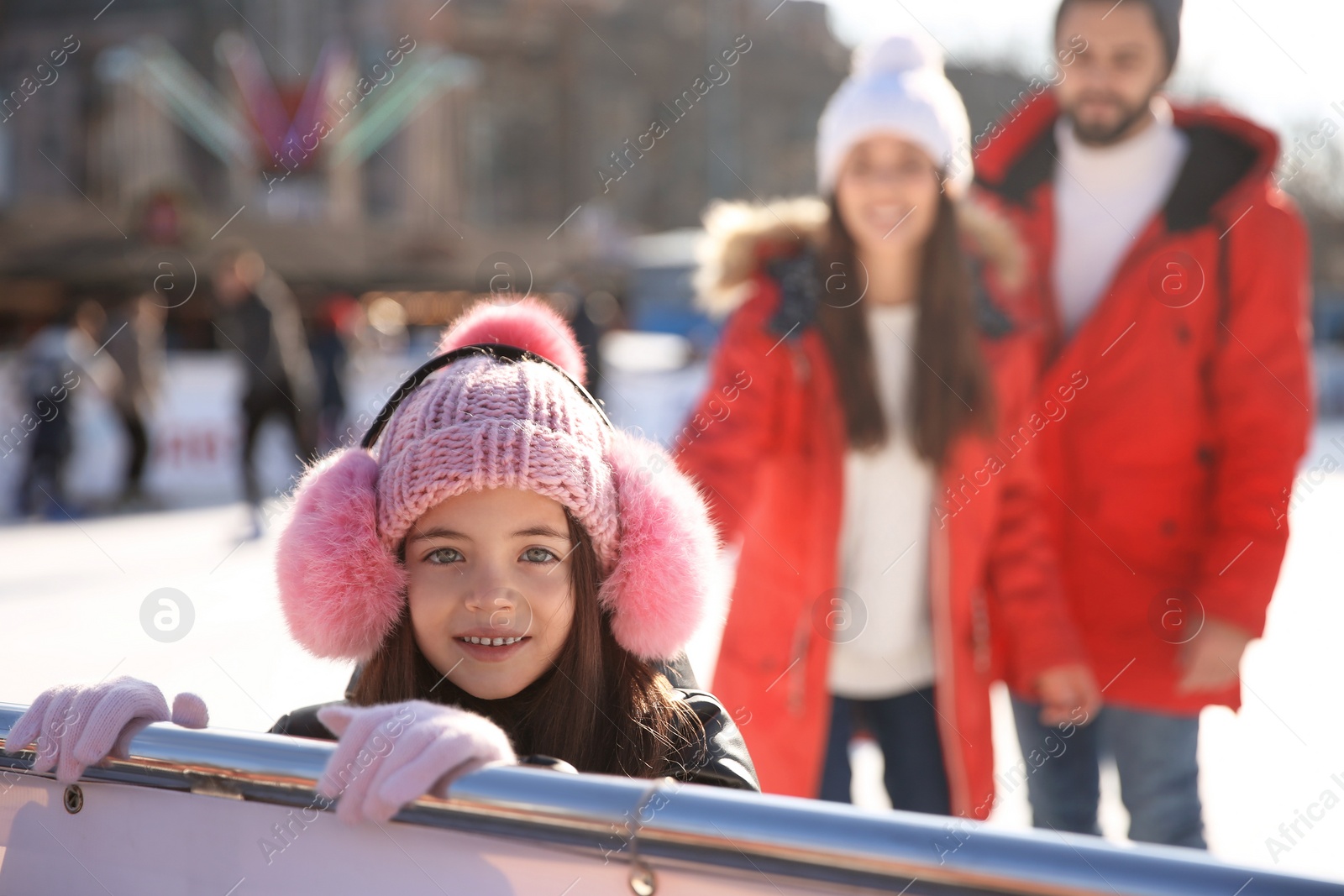 Photo of Cute little girl with her parents at outdoor ice skating rink