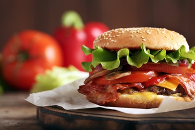 Tasty burger with bacon on wooden board, closeup. Space for text