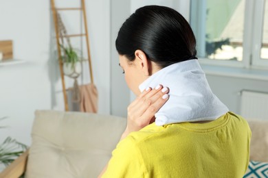 Woman using heating pad on neck at home