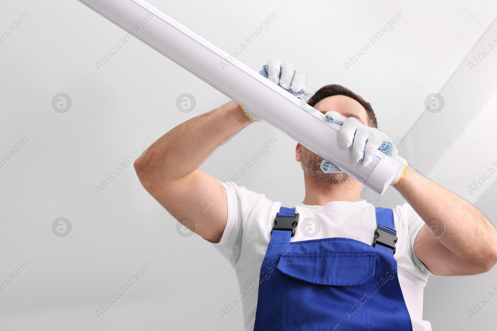 Photo of Ceiling light. Electrician installing led linear lamp indoors, low angle view. Space for text