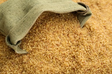 Burlap bag on pile of uncooked bulgur, closeup. Space for text