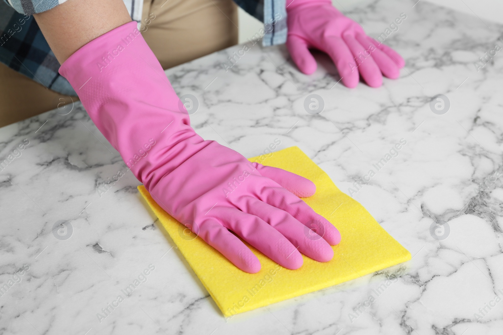 Photo of Woman in gloves wiping white marble table with rag, closeup