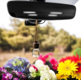 Beautiful flowers and air freshener hanging on rear view mirror in car