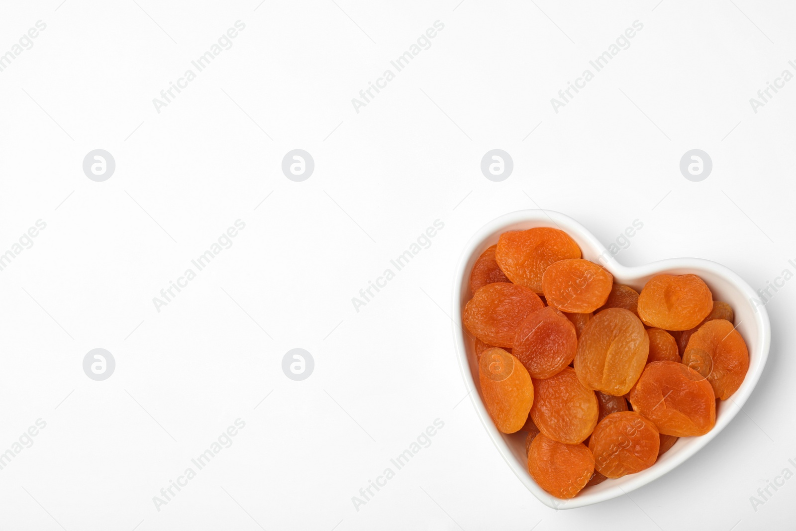 Photo of Bowl of dried apricots on white background, top view with space for text. Healthy fruit