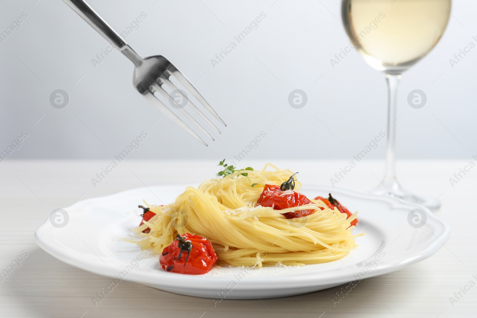 Photo of Eating tasty capellini with tomatoes and cheese at white wooden table, closeup. Exquisite presentation of pasta dish