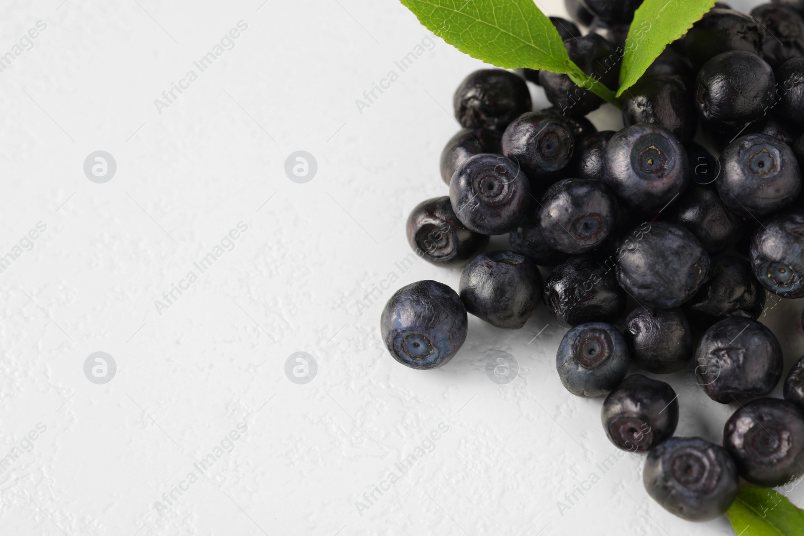 Photo of Pile of ripe bilberries and leaves on white background, closeup. Space for text