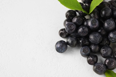 Pile of ripe bilberries and leaves on white background, closeup. Space for text