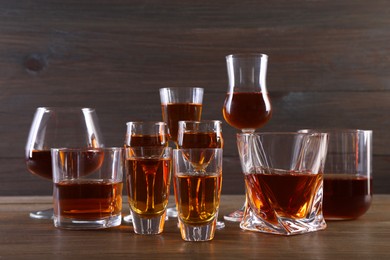 Photo of Different delicious liqueurs in glasses on wooden table