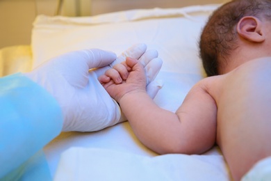 Doctor holding newborn child's hand in hospital, closeup