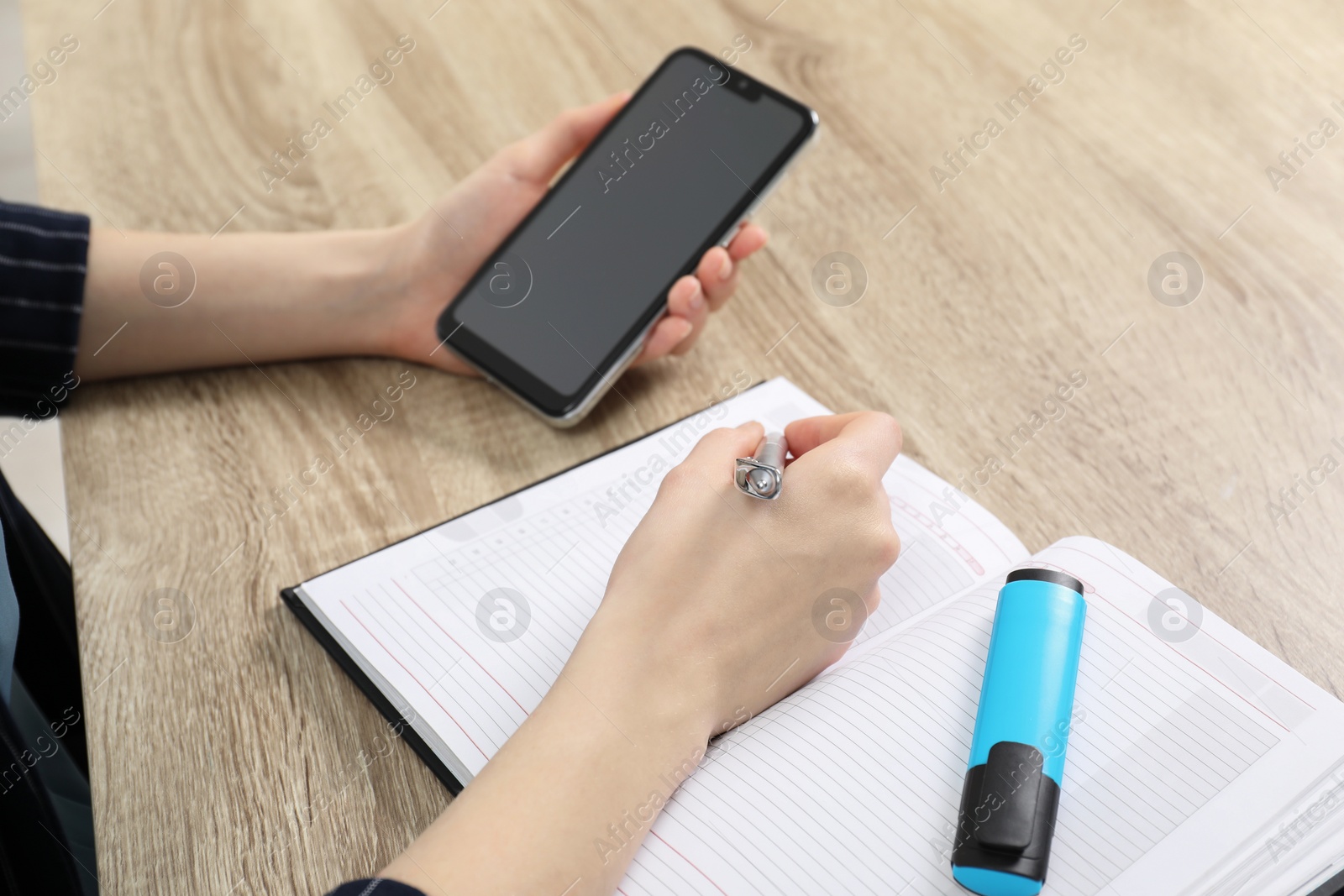 Photo of Woman taking notes while using smartphone at wooden table, closeup