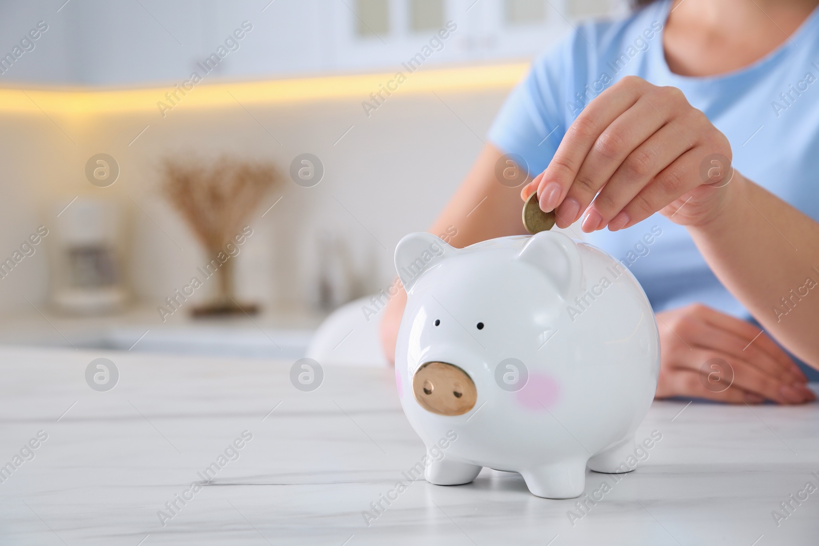 Photo of Young woman putting coin into piggy bank at table indoors, closeup and space for text. Money savings