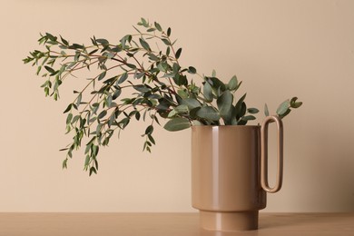 Photo of Stylish ceramic vase with eucalyptus branches on wooden table near beige wall