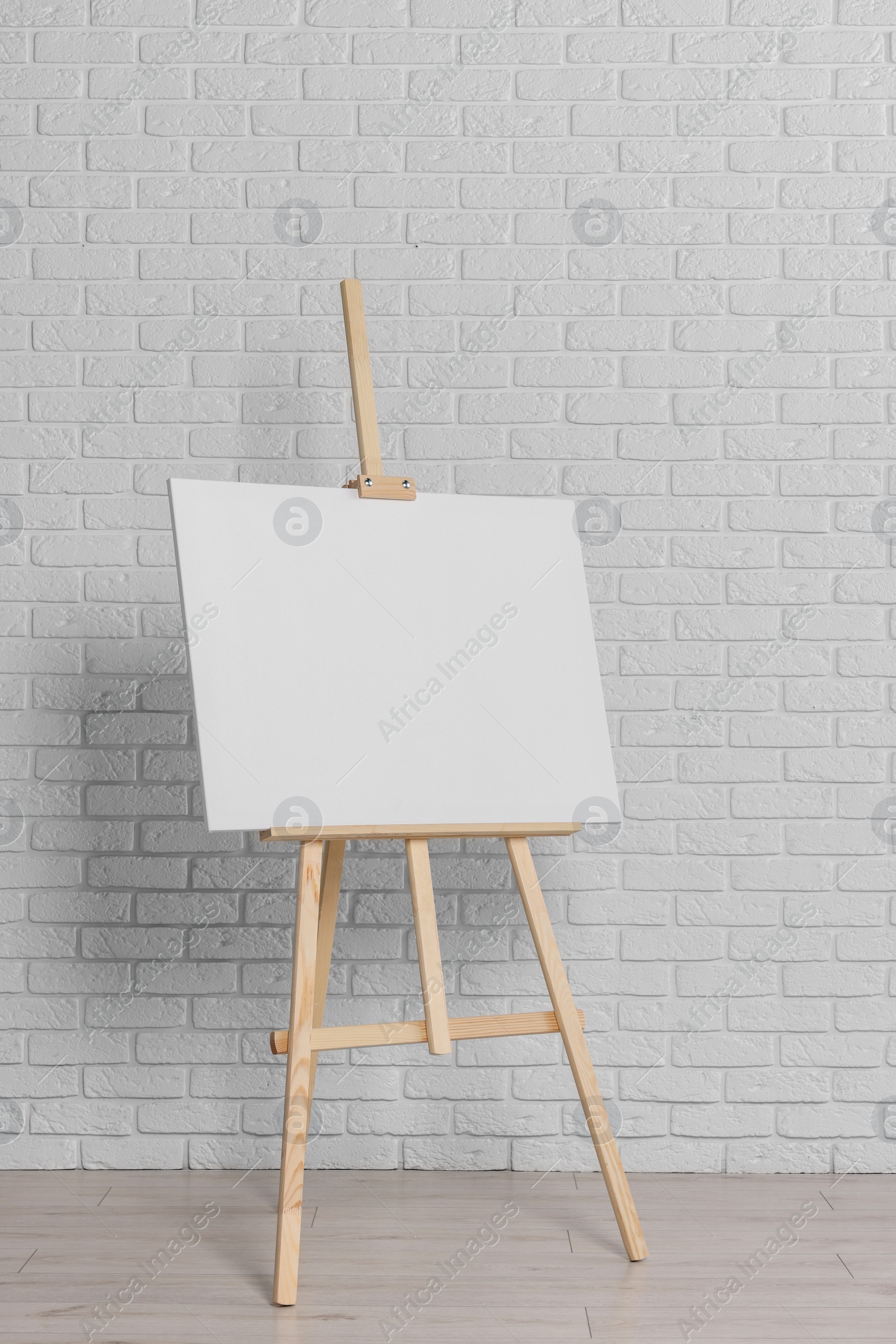 Photo of Wooden easel with blank canvas near white brick wall indoors