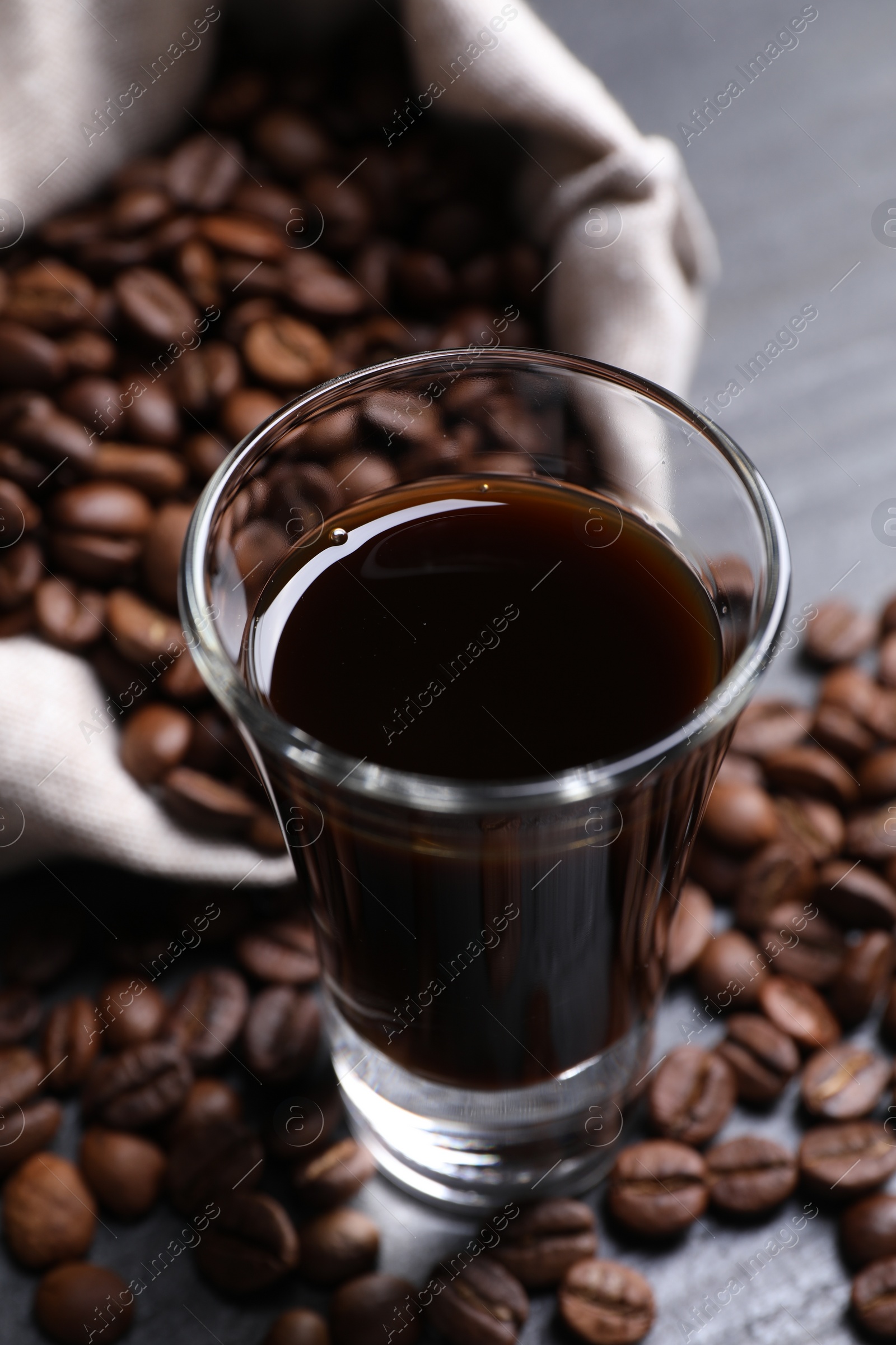 Photo of Shot glass of coffee liqueur and beans on grey table, closeup