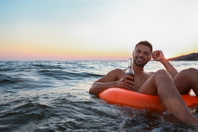 Photo of Happy young man with drink on inflatable ring in water