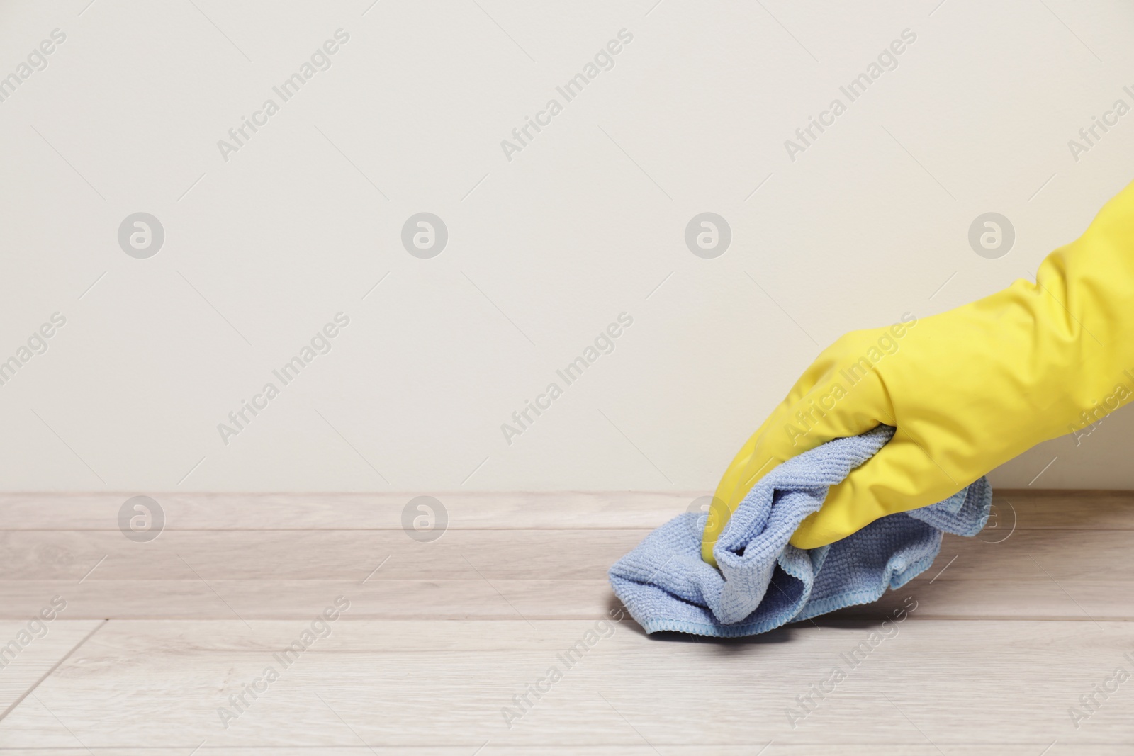 Photo of Woman in gloves cleaning plinth with cloth indoors, closeup. Space for text