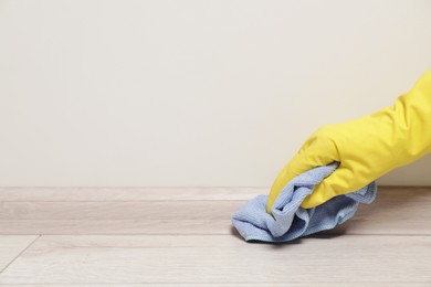 Photo of Woman in gloves cleaning plinth with cloth indoors, closeup. Space for text