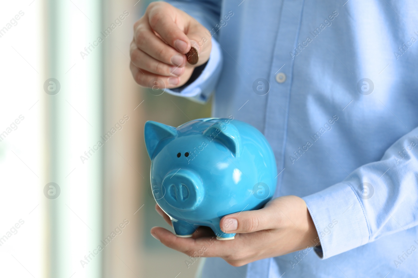 Photo of Man putting coin into piggy bank on blurred background, closeup. Money savings