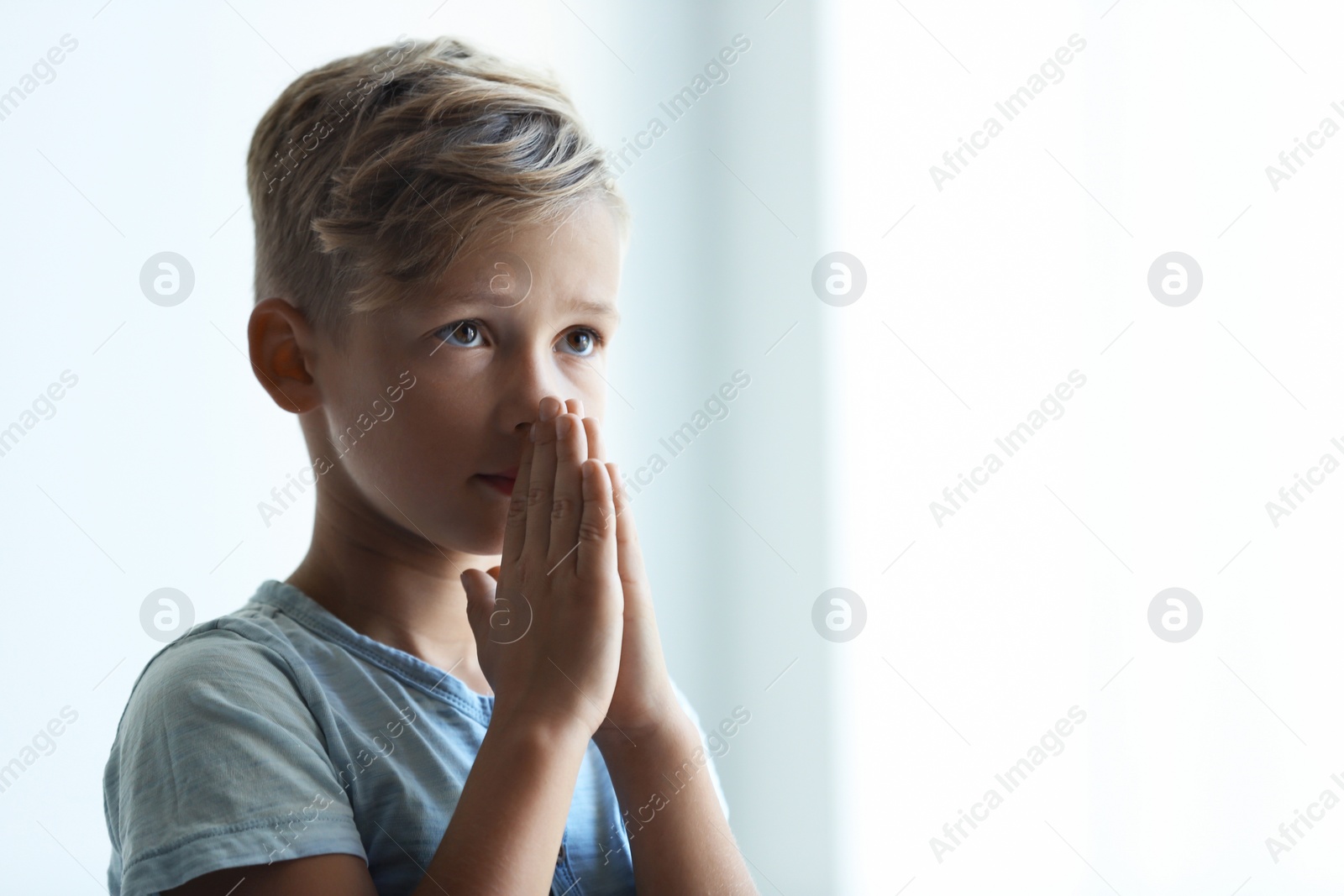 Photo of Little boy with hands clasped together for prayer on light background. Space for text