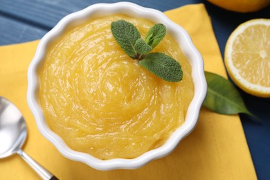 Photo of Delicious lemon curd in bowl, fresh citrus fruit and spoon on table, above view