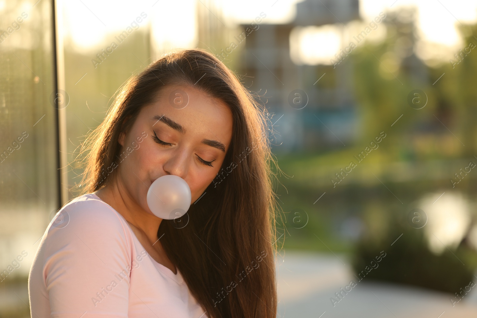 Photo of Beautiful young woman blowing bubble gum outdoors. Space for text