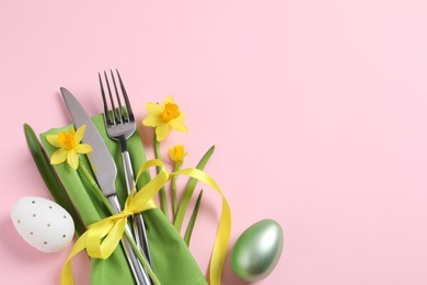 Photo of Cutlery set, Easter eggs and narcissuses on pale pink background, flat lay with space for text. Festive table setting