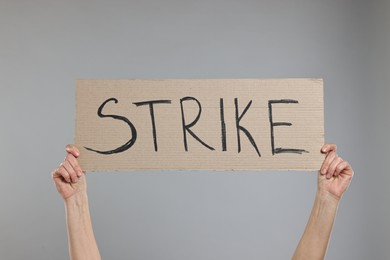 Photo of Woman holding cardboard banner with word Strike on grey background, closeup