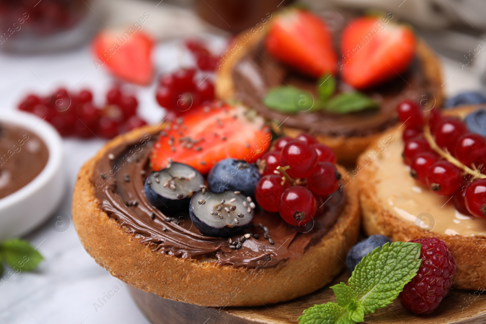 Photo of Tasty organic rusks with different toppings and ingredients on white table, closeup