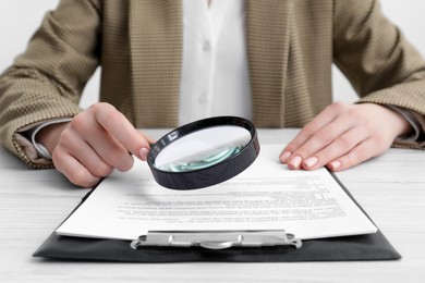 Photo of Woman looking at document through magnifier at wooden table, closeup. Searching concept