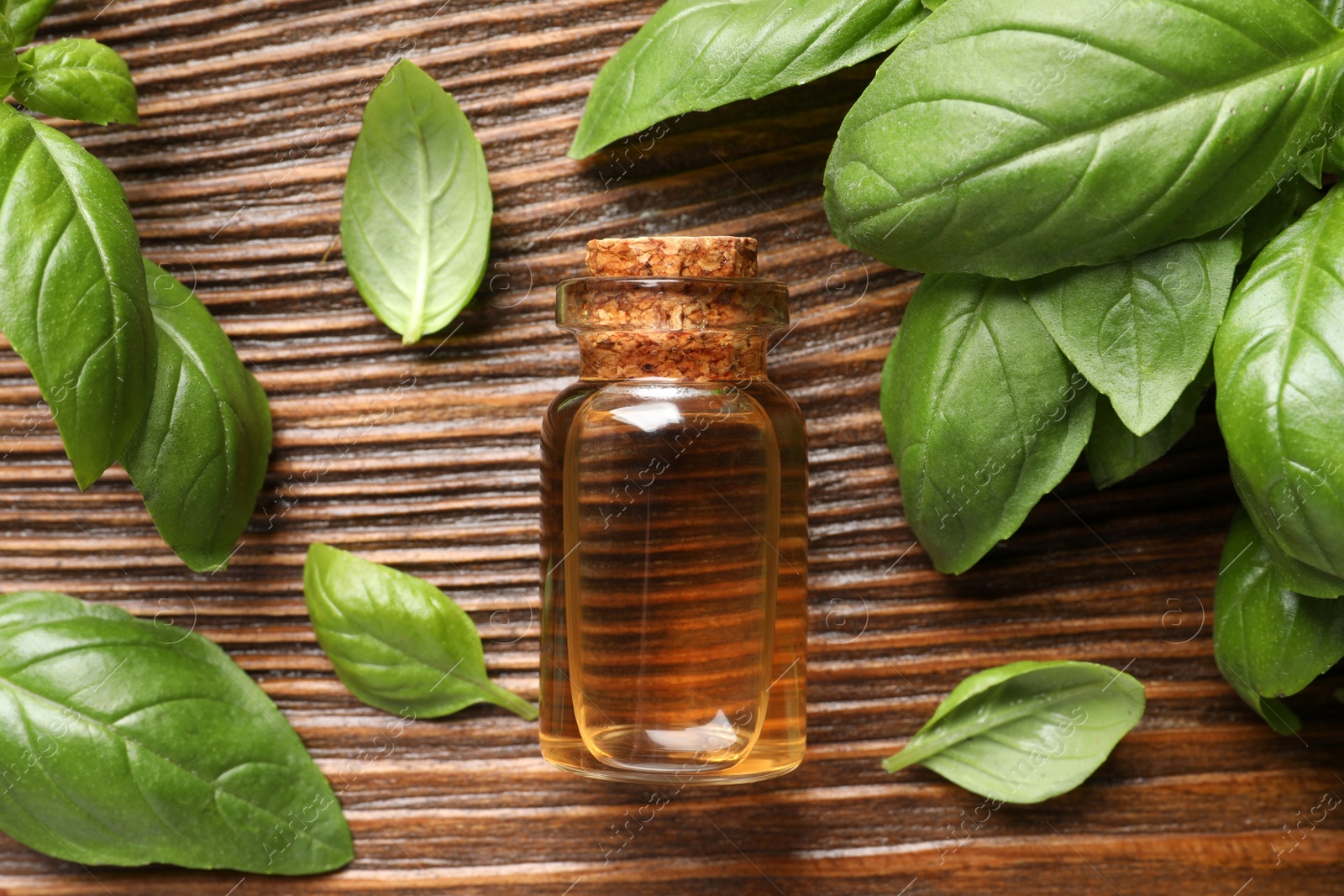 Photo of Glass bottle of basil essential oil and leaves on wooden table, flat lay